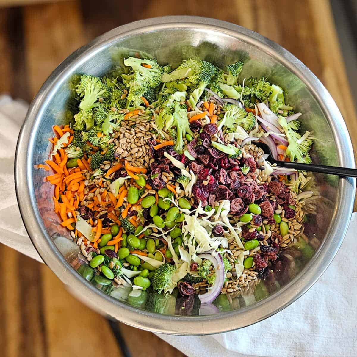 The ingredients for the easy Asian broccoli crunch salad in a bowl with a spoon being combined.