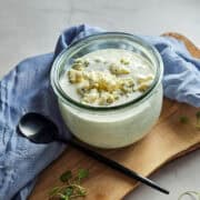 Blue cheese dressing in a glass jar with crumbles on top, with a spoon.